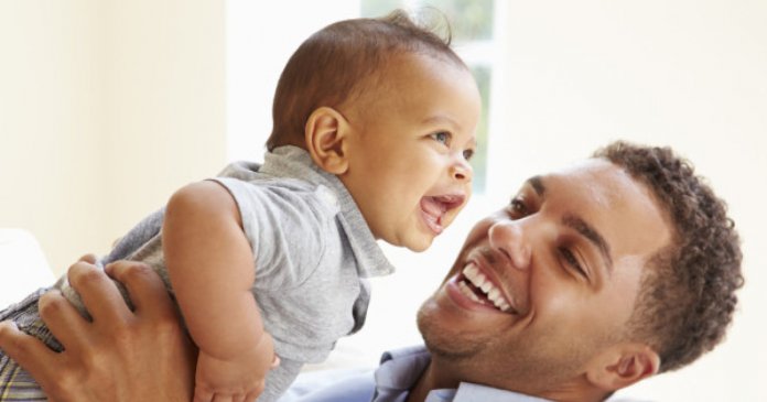 Smiling Father Playing With Baby Son At Home