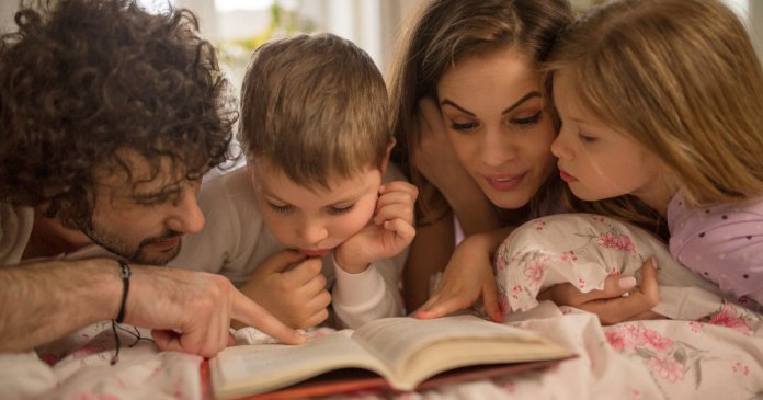 Happy family reading a story together in bed.