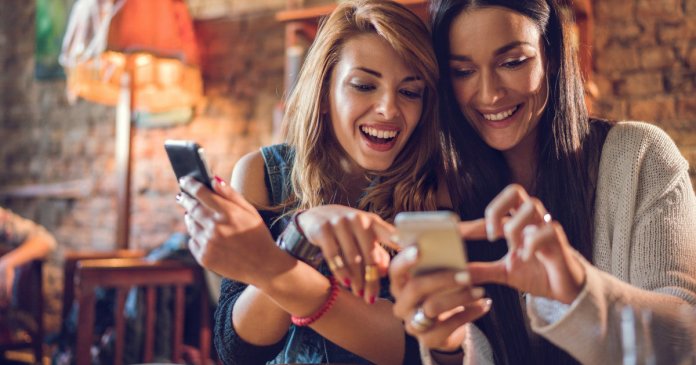Happy female friends reading a text message on cell phone.