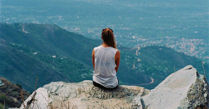 Rear View Of Woman Sitting On Mountain Top