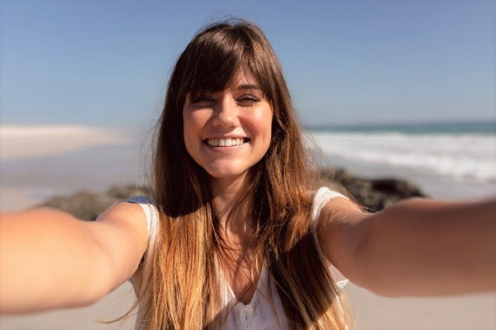 mulher-bonita-que-olha-a-camera-na-praia-na-luz-do-sol_107420-9980