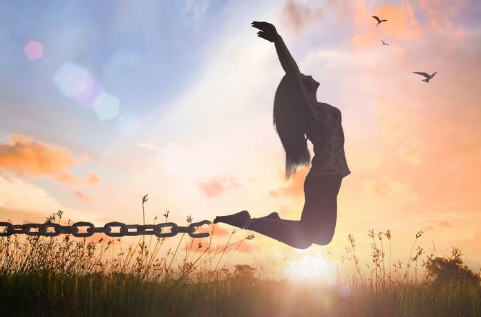 International day for the remembrance of the slave trade and its abolition concept: Silhouette of a woman jumping and broken chains at orange meadow autumn sunset with her hands raised